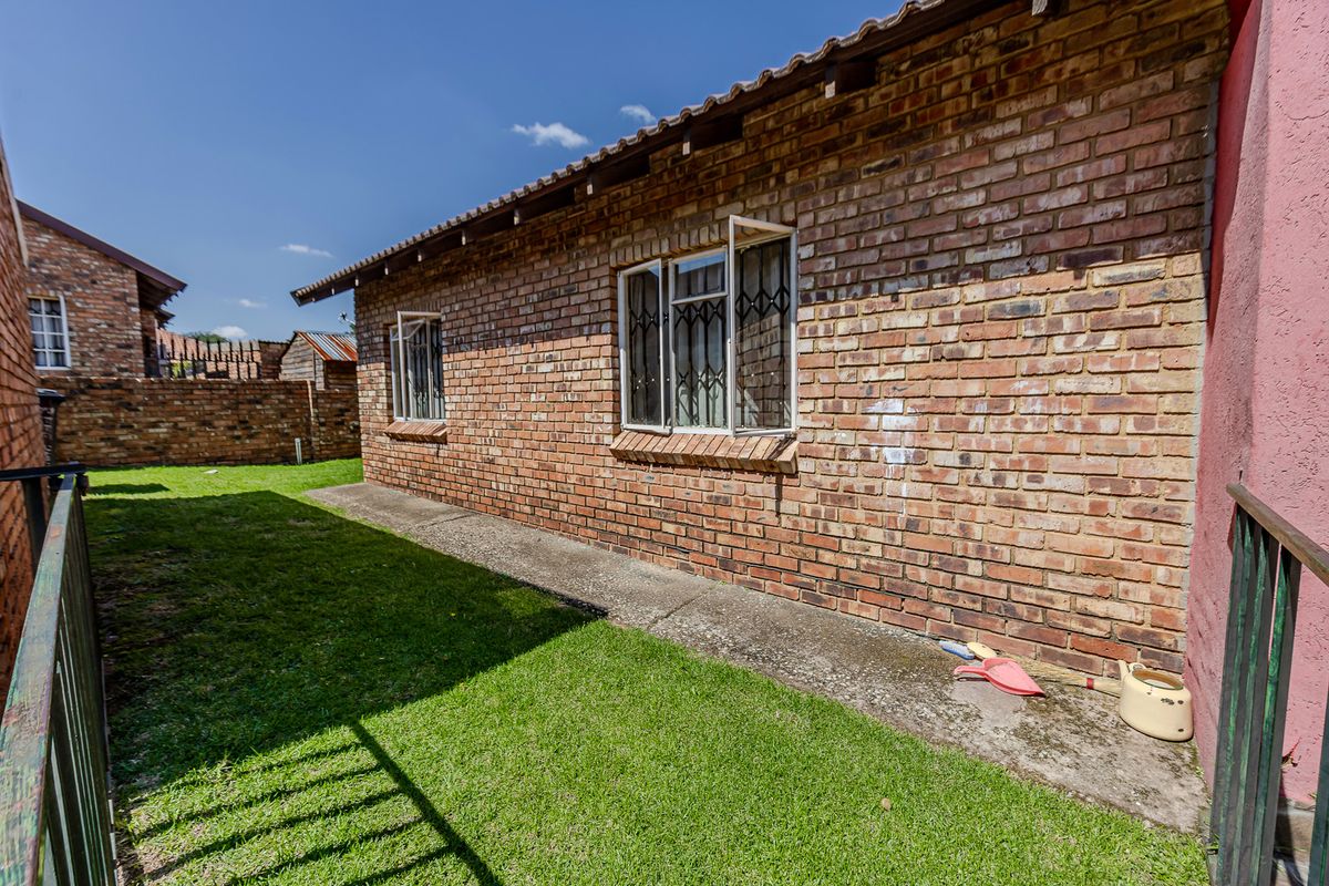 Rear exterior view of the townhouse featuring a face brick facade, tiled roof, security bars on windows, and a small private lawn area.