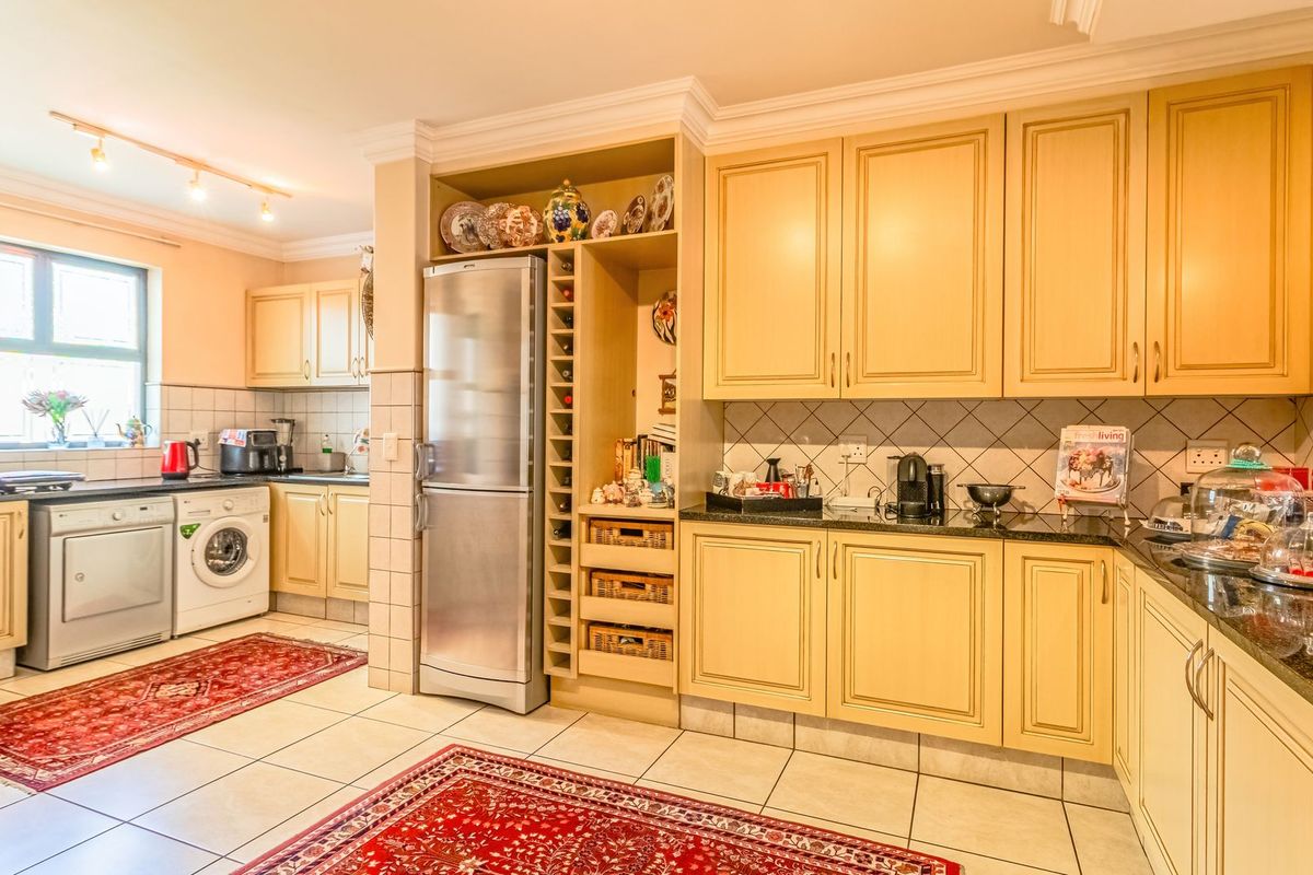 A spacious kitchen featuring light-toned cabinetry, granite countertops, tiled backsplash, and integrated storage, offering a functional layout with dedicated laundry area space.
