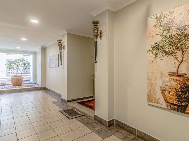 A well-lit, spacious hallway featuring neutral ceramic floor tiles, coved ceiling cornices, and decorative wall-mounted sconces leading toward a bright balcony area.