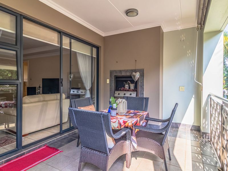 Covered balcony featuring a built-in braai, tiled flooring, and a stainless steel balustrade, providing a seamless transition to the interior living space.