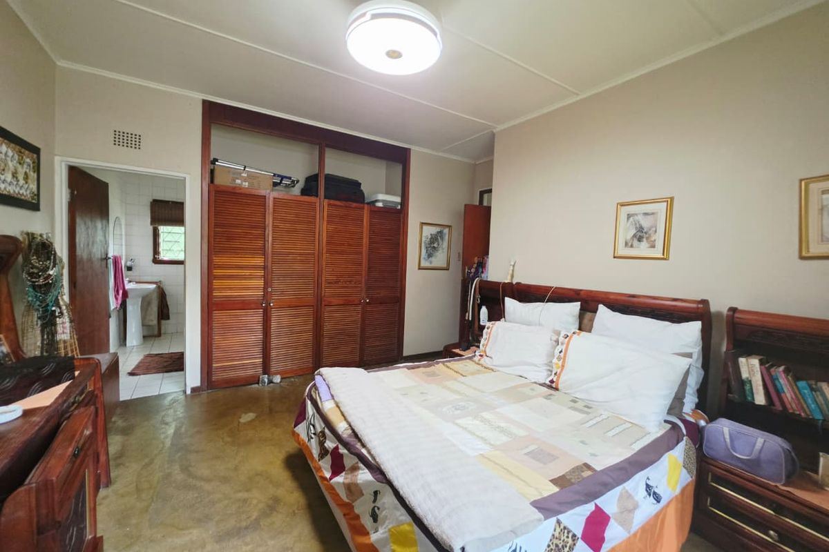Spacious bedroom featuring built-in wooden wardrobes, a ceiling fan, and direct access to an en-suite bathroom with concrete flooring throughout.