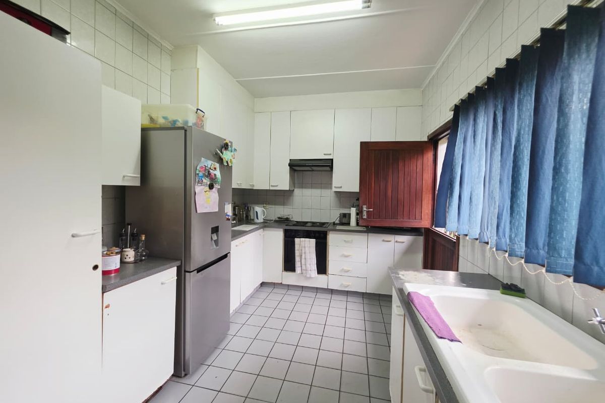 Functional kitchen featuring white built-in cabinetry, a double basin sink, tiled flooring, and integrated oven with extractor fan.