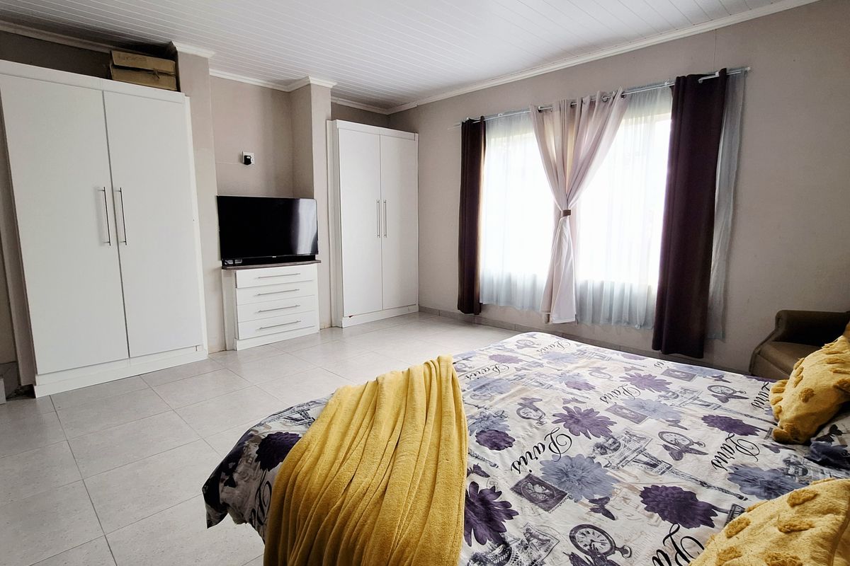 A well-maintained bedroom featuring built-in white wardrobes, tiled flooring, and a tongue-and-groove ceiling, offering a clean and functional living space.