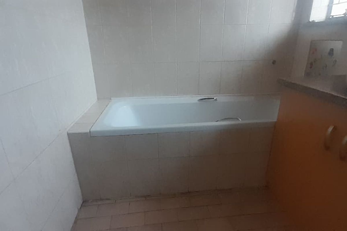A dated bathroom featuring a built-in bathtub, vanity cabinet with basin, and tiled surfaces throughout.