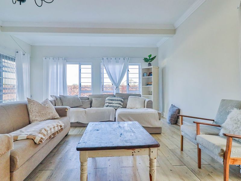A bright and spacious living room featuring light-toned timber flooring, large windows, and a sliding door leading to the exterior.
