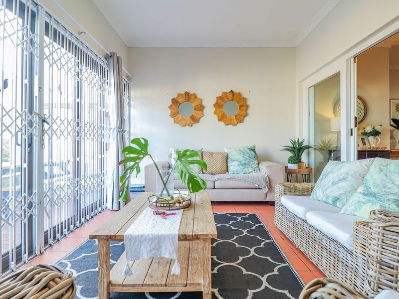 A bright sunroom or enclosed patio featuring tiled flooring and large sliding glass doors with security gates, providing access to the outdoor area.