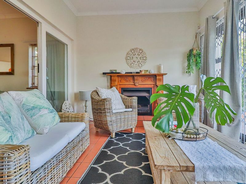 A sunlit living room featuring a traditional wooden fireplace mantel, terracotta floor tiles, and large sliding glass doors leading to the exterior.
