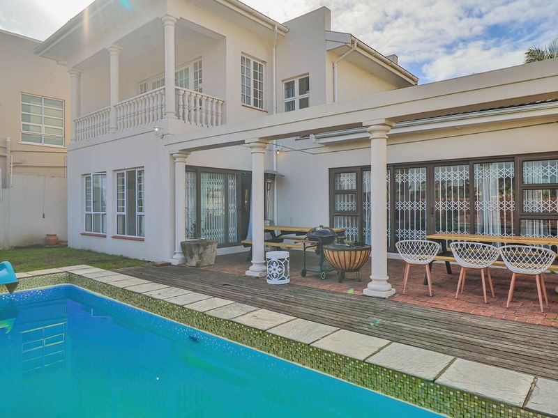Rear exterior view featuring a swimming pool, a covered patio area with columns, and a two-story residential building with a balcony.