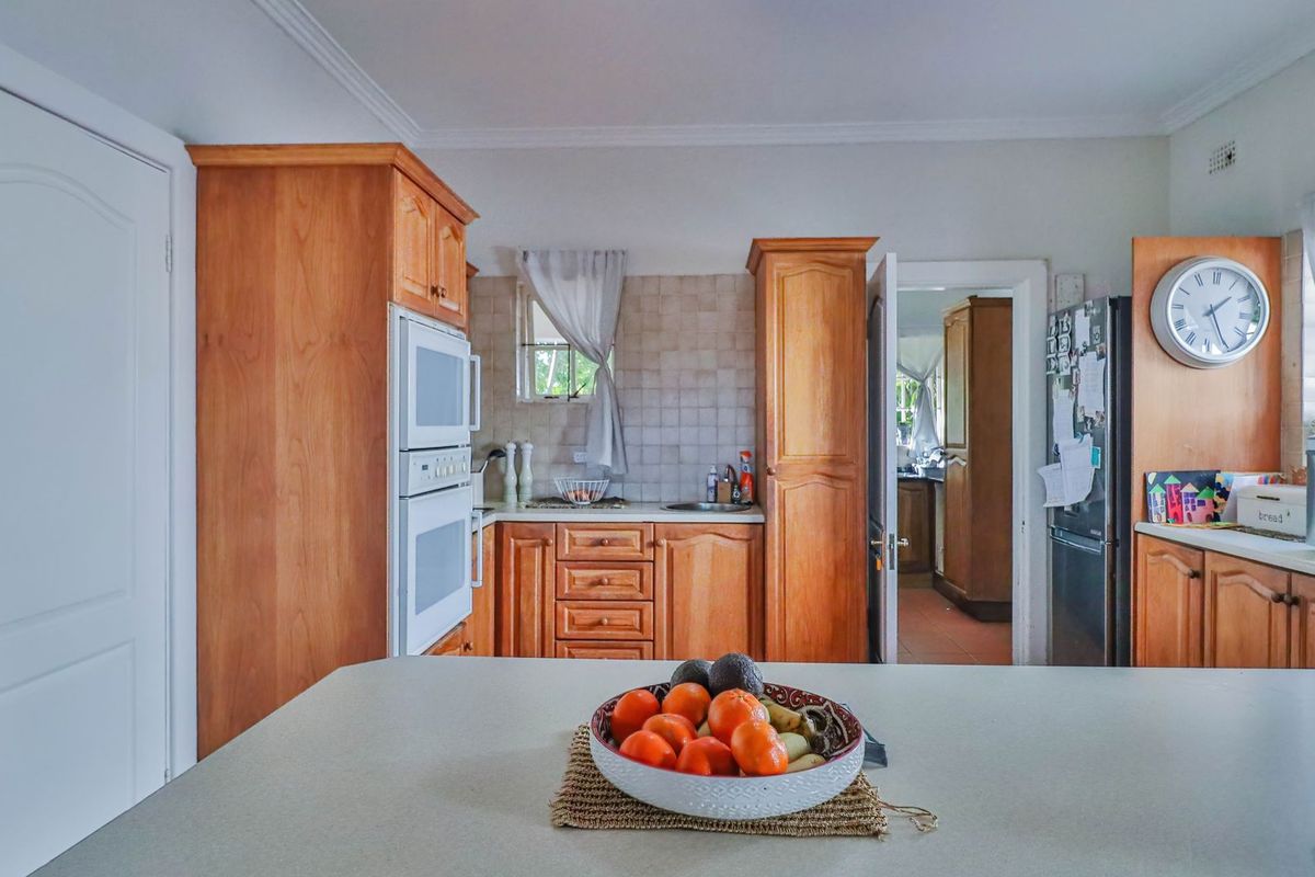 A functional kitchen featuring traditional wooden cabinetry, built-in oven, and a central island, with an adjacent scullery area visible through the doorway.