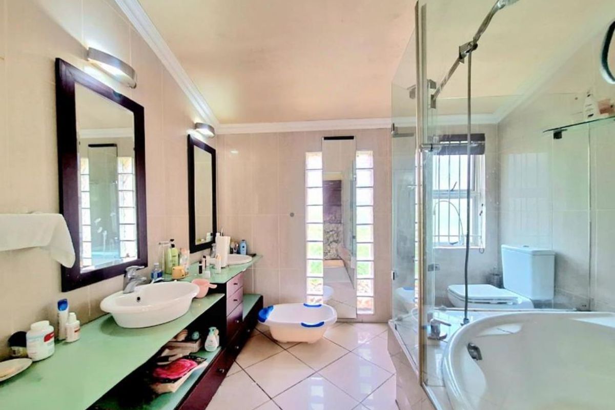 Spacious bathroom featuring a double vanity with vessel sinks, a glass-enclosed shower, a bathtub, and a toilet, finished with neutral wall tiles.
