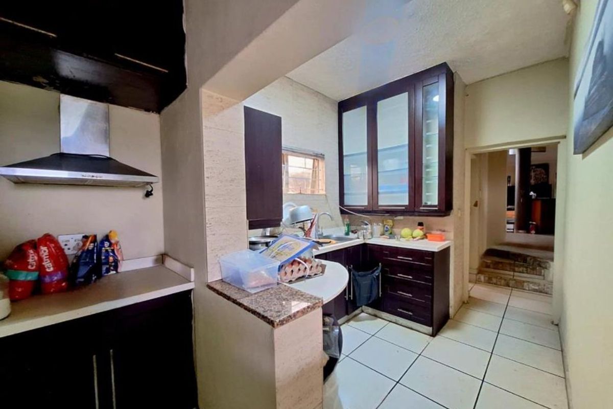 Compact kitchen featuring dark wood cabinetry, granite countertops, stainless steel extractor fan, and tiled flooring with a functional layout.