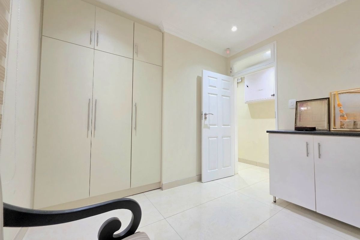 A clean bedroom featuring neutral tiled flooring, ample built-in cupboard storage, and a classic panel door leading to an adjacent space.