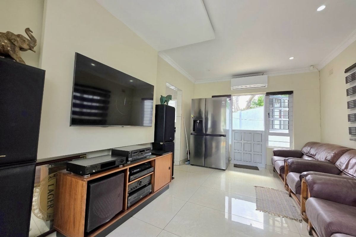 A bright living room featuring tiled flooring, a recessed ceiling, and a wall-mounted split-system air conditioner, providing a comfortable and functional living space.