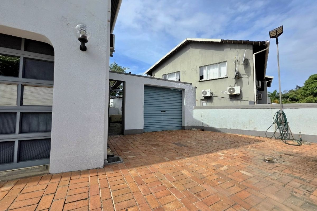 Rear courtyard area featuring brick paving, a roller shutter garage door, and boundary walling with mounted air conditioning units.