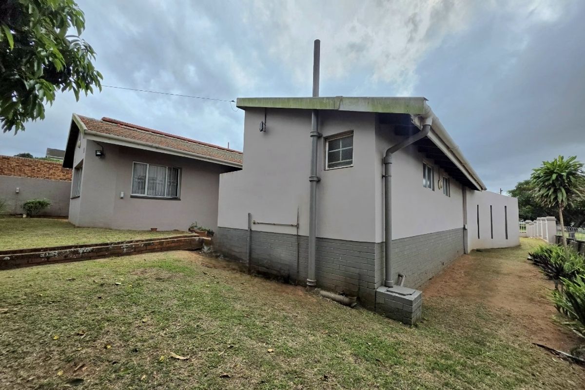 Rear view of the property showing exterior brick walls, tiled roofing, and drainage systems, set within a grassed garden area.