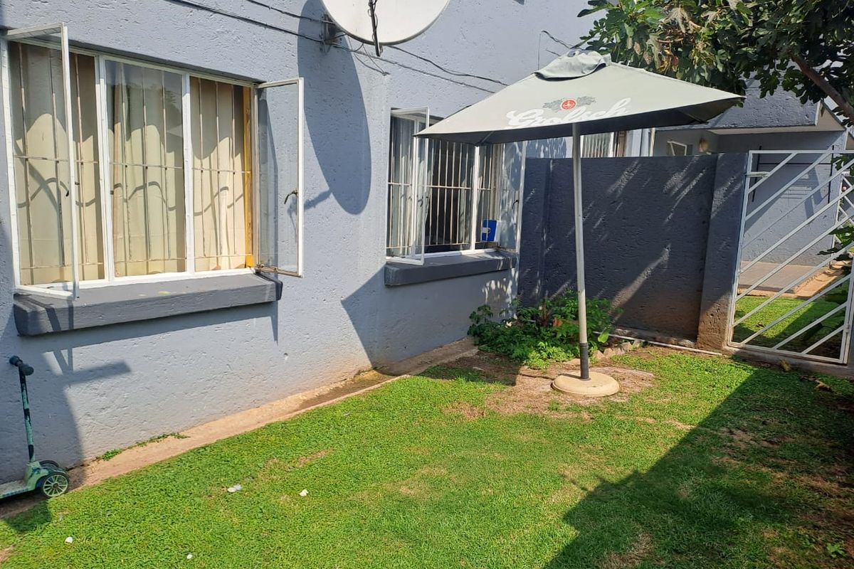 Rear exterior view of the townhouse featuring a small private garden, security bars on windows, and boundary walling.