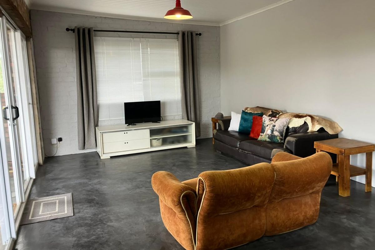 A spacious living room featuring polished concrete floors, an exposed brick feature wall, and large sliding glass doors providing natural light.