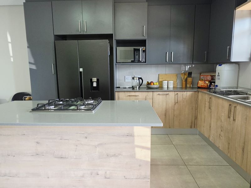 Modern kitchen featuring a central island with a gas hob, ample built-in cabinetry, double sink, and tiled flooring.