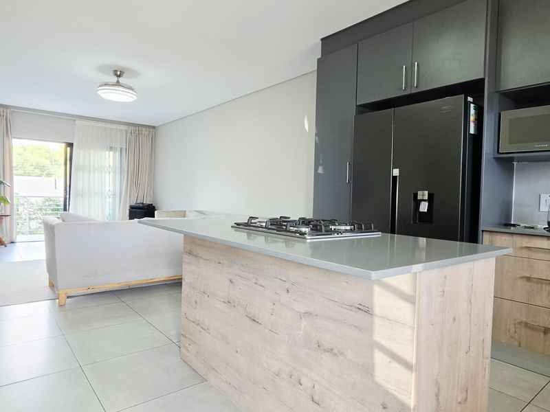 Modern open-plan living area featuring a contemporary kitchen with stone countertops, gas hob, built-in microwave, and seamless flow to the patio.