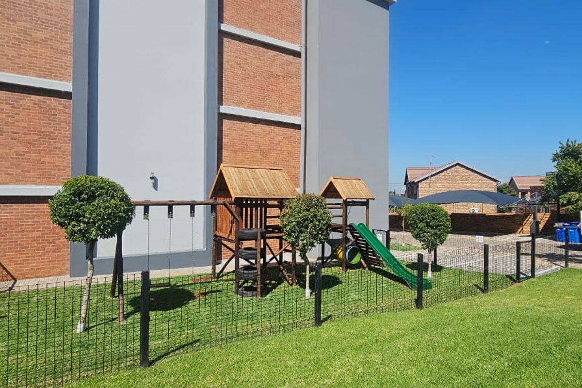Rear exterior view of the townhouse featuring a brick and rendered facade, metal balcony railings, and a well-maintained lawn with perimeter fencing.