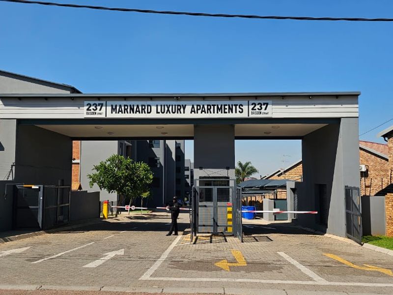 The main entrance to the Marnard Luxury Apartments complex, featuring a secure gatehouse, automated boom gates, and paved driveway access.