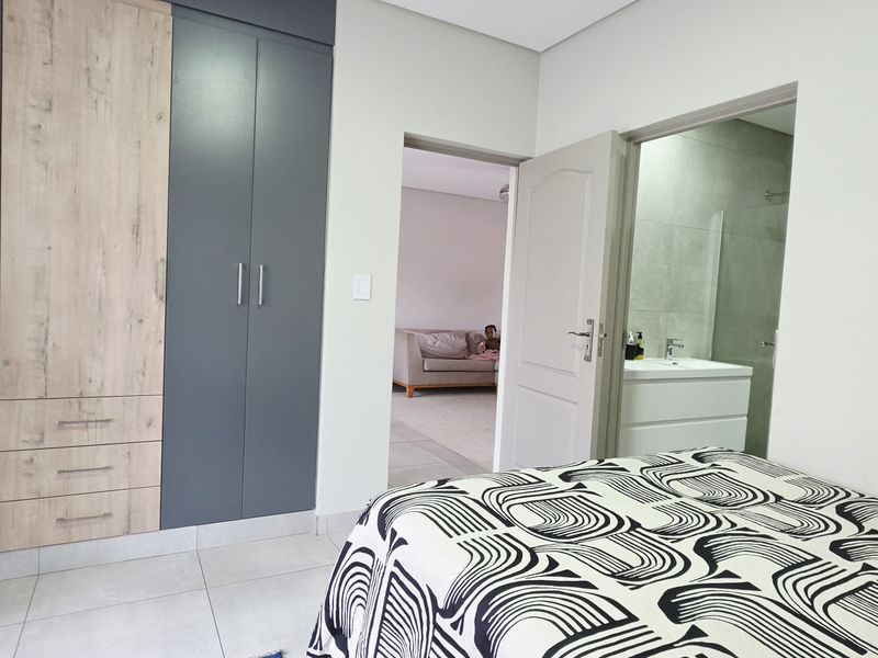 A well-maintained bedroom featuring modern two-tone built-in cupboards, tiled flooring, and direct access to an en-suite bathroom.