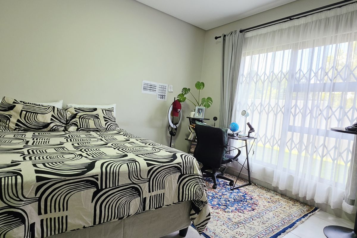 A well-lit bedroom featuring a large window with a security gate, neutral wall tones, and tiled flooring.