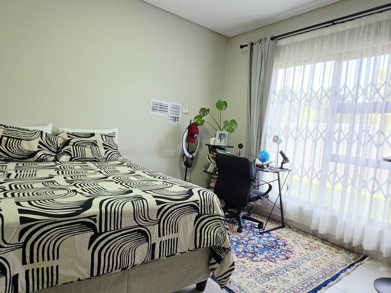 A well-lit bedroom featuring a large window with a security gate, neutral wall tones, and tiled flooring.