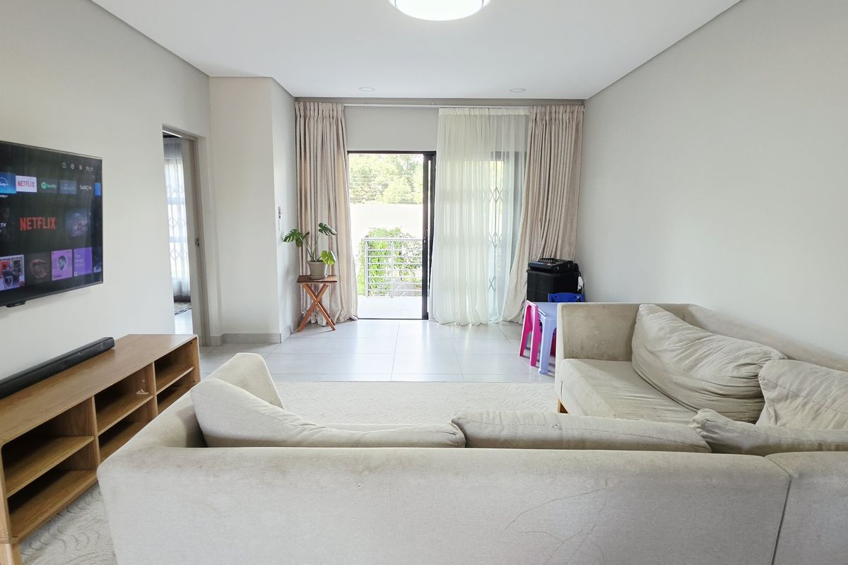 A bright and spacious living room featuring tiled flooring, recessed lighting, and a sliding glass door providing access to an outdoor balcony area.