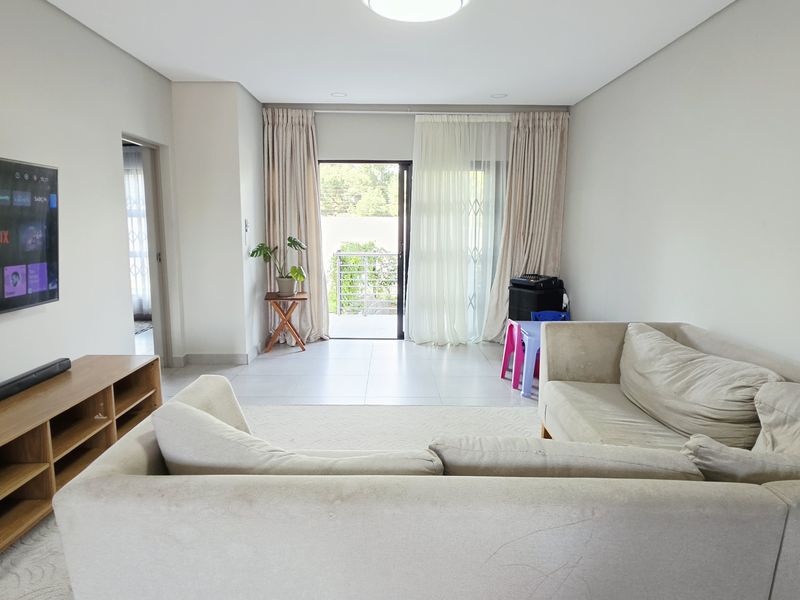 A bright and spacious living room featuring tiled flooring, recessed lighting, and a sliding glass door providing access to an outdoor balcony area.