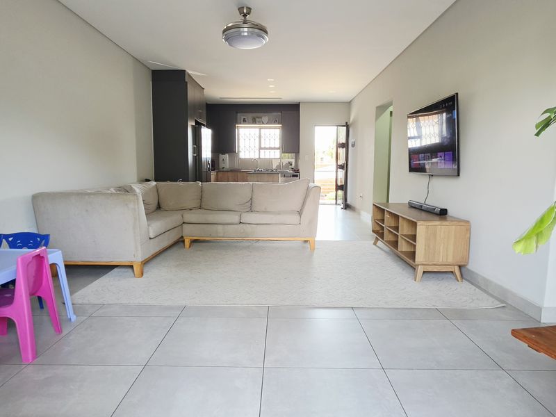 Spacious open-plan living area featuring large format floor tiles, a ceiling fan, and a seamless transition to the kitchen space.