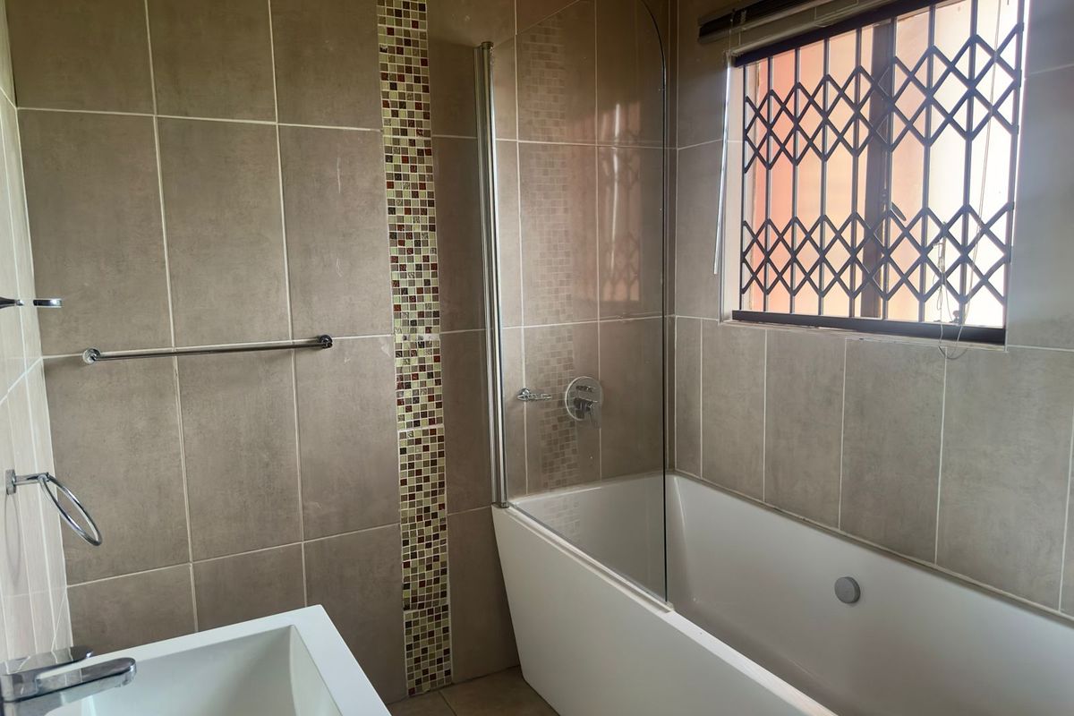 A functional bathroom featuring a built-in bathtub with a glass shower screen, wall-mounted shower head, and decorative mosaic tile accents.