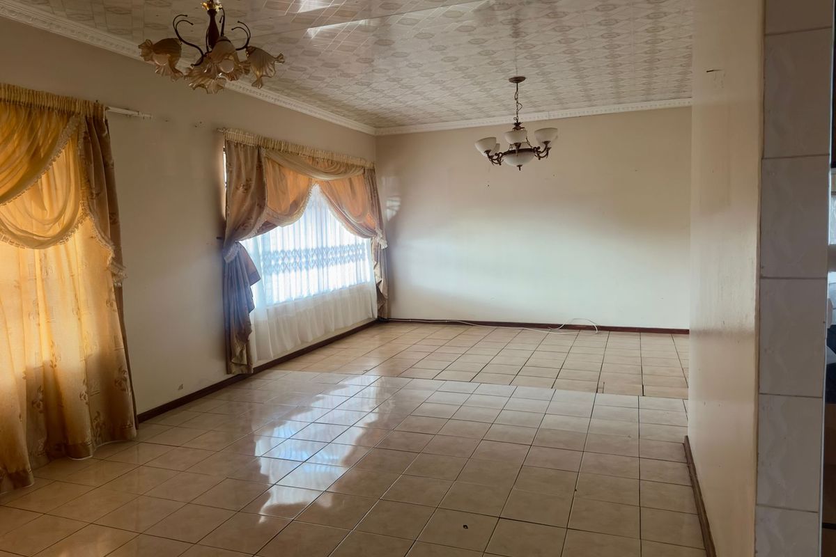 A spacious, empty living area featuring tiled flooring, decorative ceiling tiles, and classic light fixtures, offering a blank canvas for renovation.