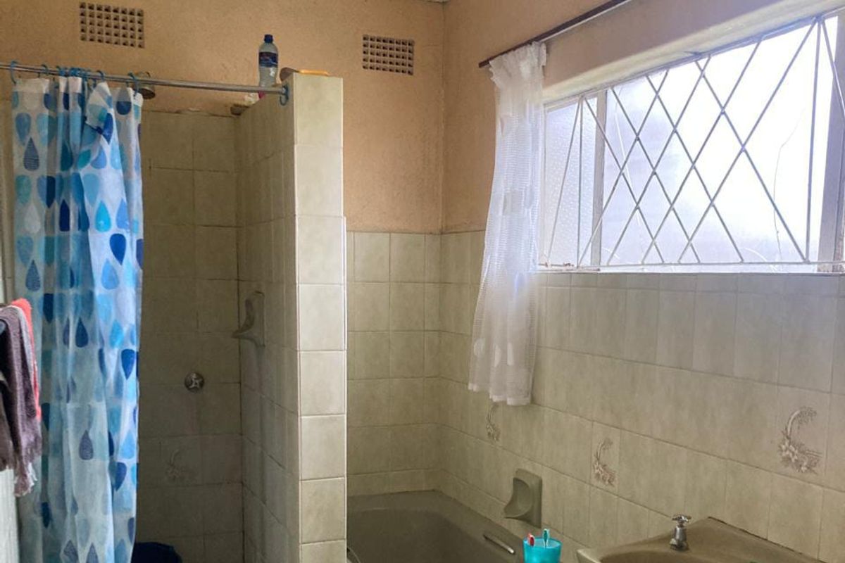 A dated bathroom featuring a built-in shower cubicle, a standard bathtub, and a pedestal basin with tiled walls and a window.