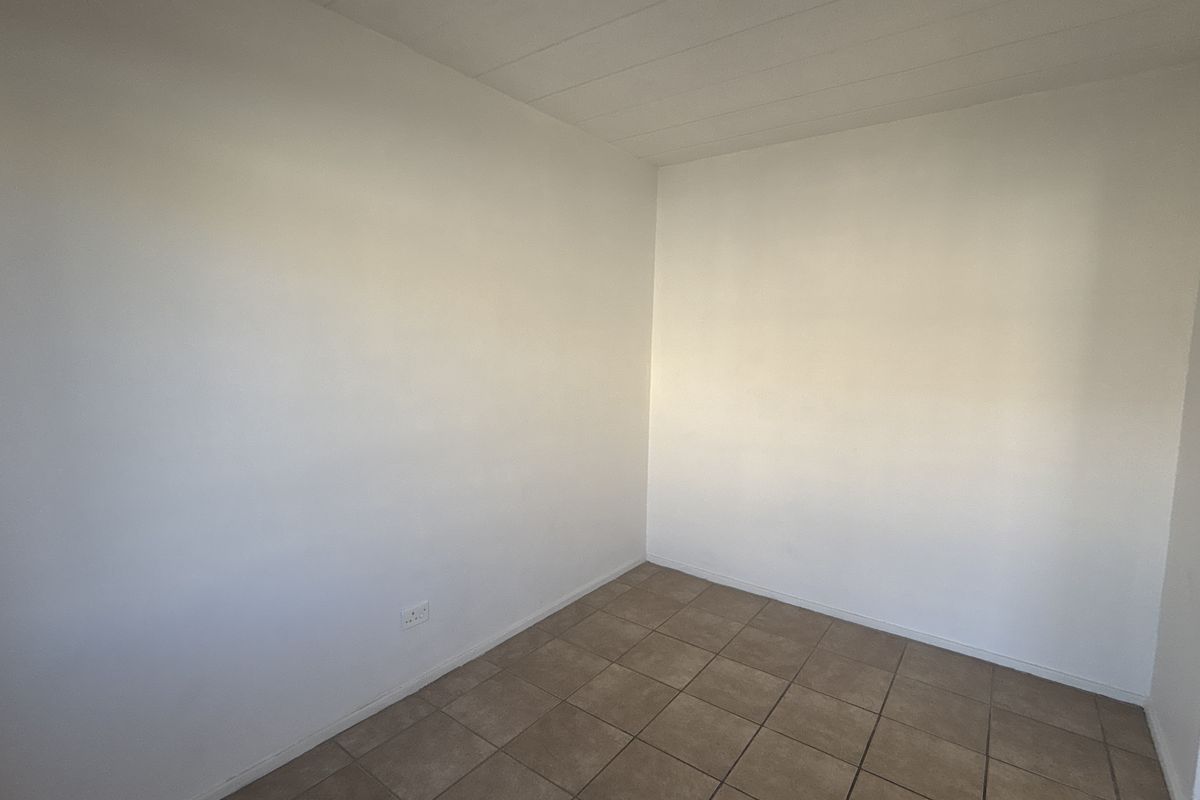A vacant bedroom featuring neutral white walls and tiled flooring, providing a clean and versatile space ready for personalization.