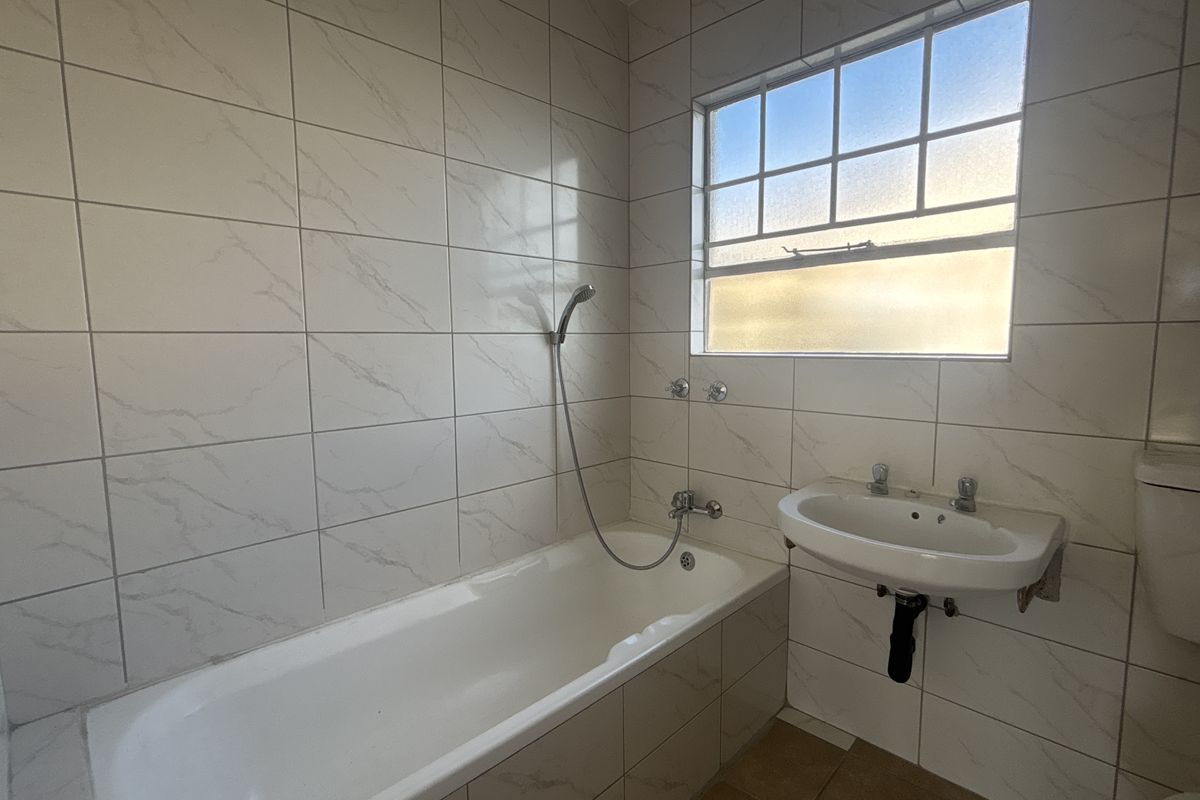 A functional bathroom featuring a bathtub with a handheld shower attachment, a wall-mounted basin, and neutral marble-look wall tiling.