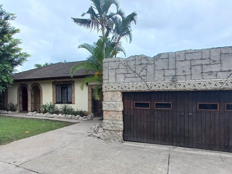 Front exterior view of the property featuring a unique stone-clad garage facade, concrete driveway, and established garden area.