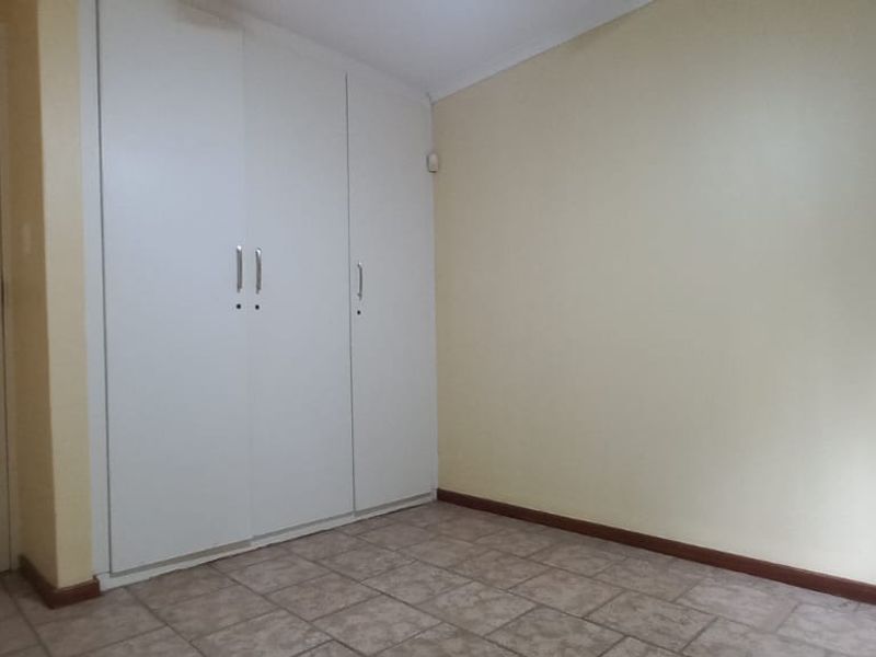 A clean, empty bedroom featuring neutral walls, tiled flooring, and built-in storage cupboards.