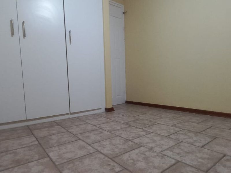 An empty bedroom featuring tiled flooring and built-in cupboards with a neutral wall finish.
