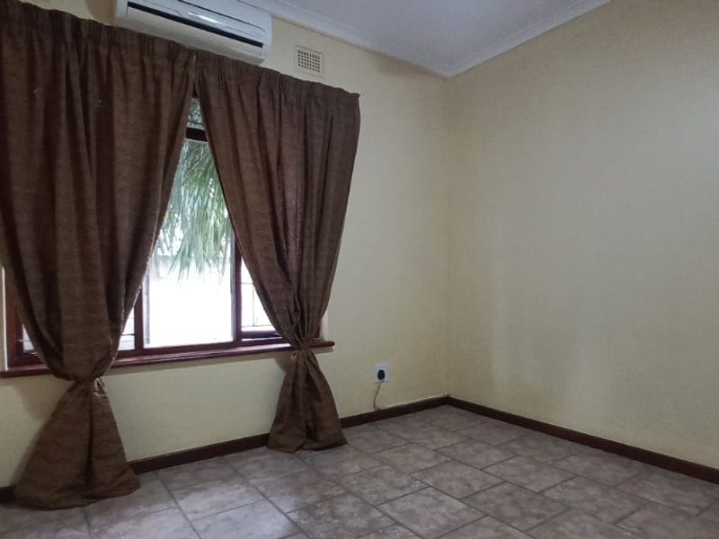A clean, empty bedroom featuring tiled flooring, neutral wall paint, and a wall-mounted air conditioning unit.