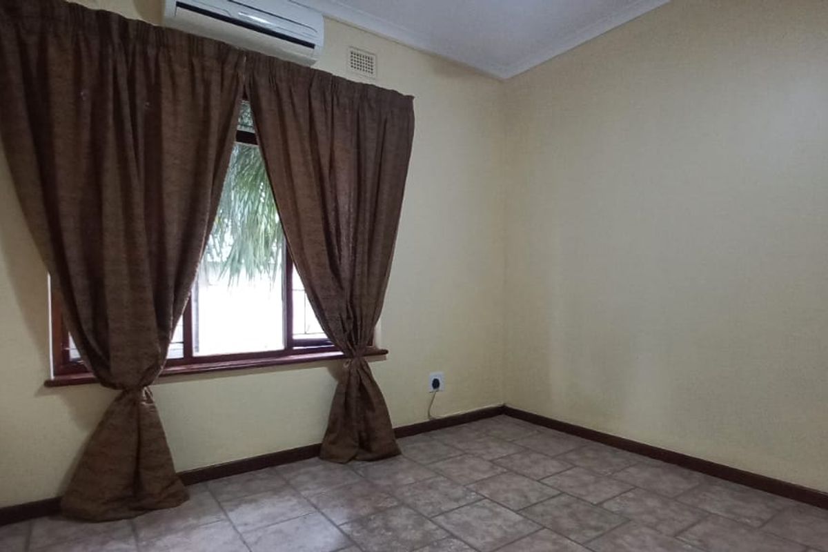 A clean, empty bedroom featuring tiled flooring, neutral wall paint, and a wall-mounted air conditioning unit.