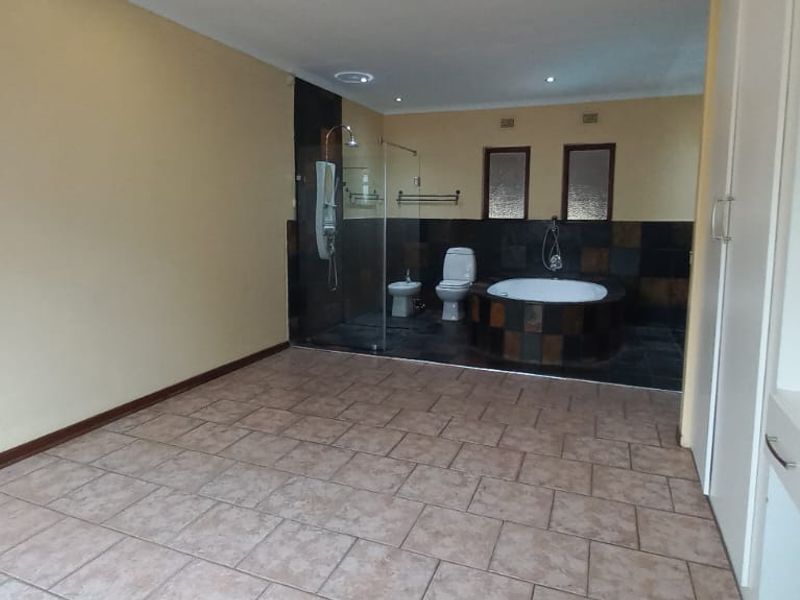 Spacious bathroom featuring tiled flooring, a walk-in shower, a circular bathtub, a toilet, a bidet, and built-in storage cabinetry.