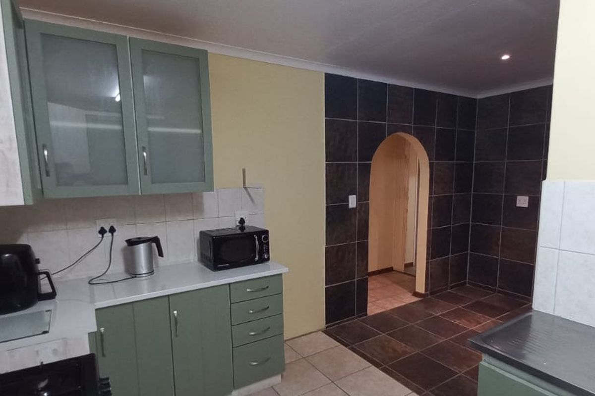 A functional kitchen featuring green cabinetry, tiled splashbacks, and an arched doorway leading to an adjacent space with dark floor tiles.