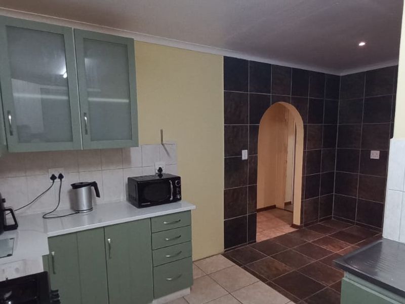 A functional kitchen featuring green cabinetry, tiled splashbacks, and an arched doorway leading to an adjacent space with dark floor tiles.