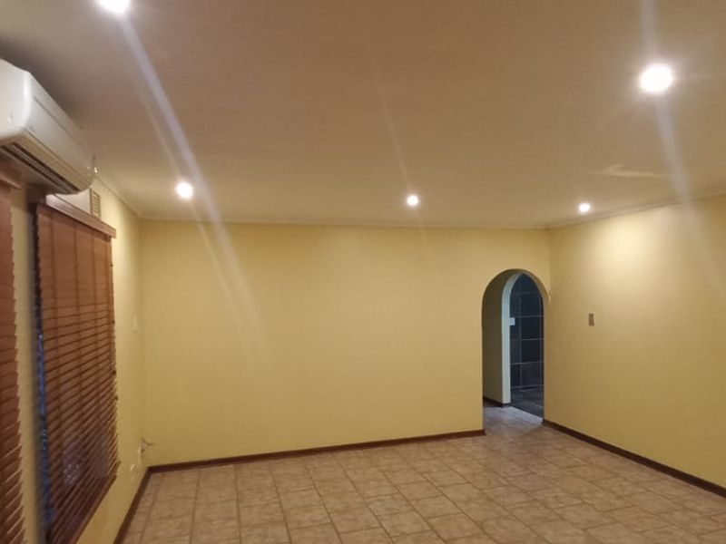 An empty living room featuring tiled flooring, recessed downlighting, a wall-mounted air conditioning unit, and an arched doorway leading to an adjacent space.