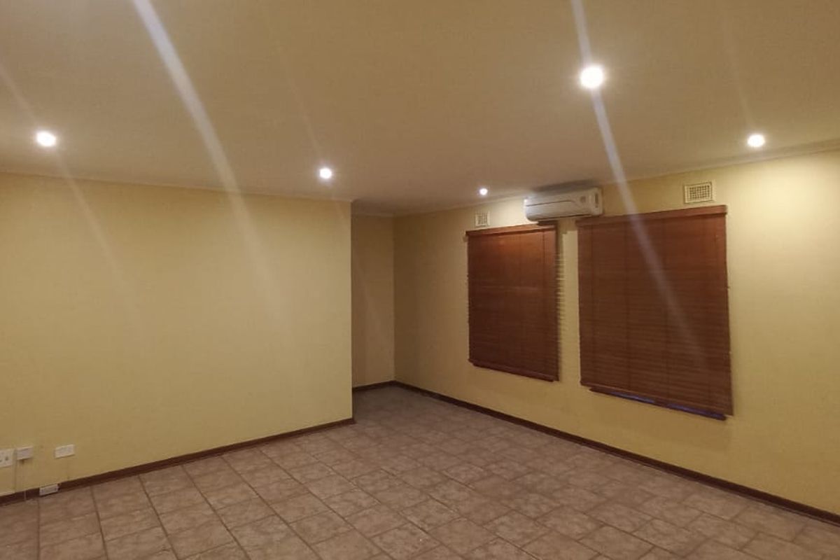 A spacious, empty living area featuring tiled flooring, recessed downlighting, and a wall-mounted split-system air conditioner.