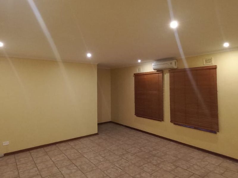 A spacious, empty living area featuring tiled flooring, recessed downlighting, and a wall-mounted split-system air conditioner.