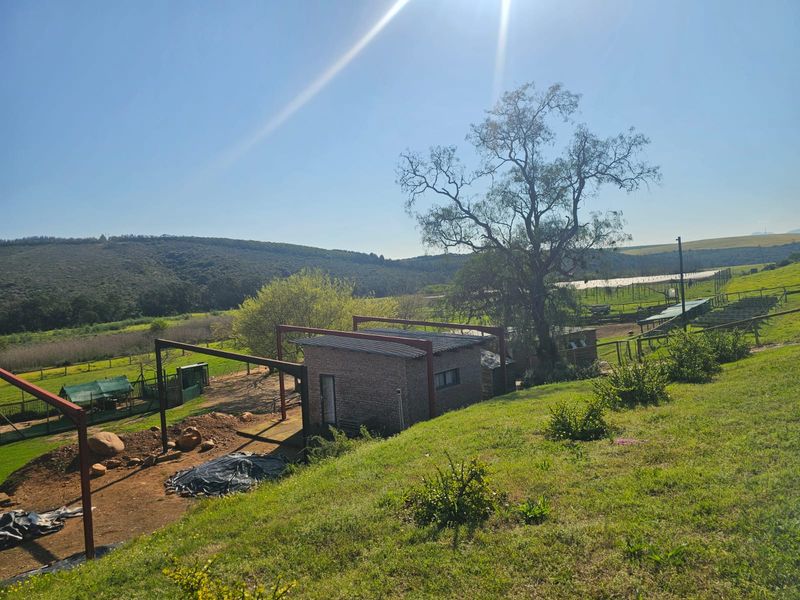 An elevated view of a farm property featuring a brick structure with exposed metal framing, set against a backdrop of rolling hills and open land.
