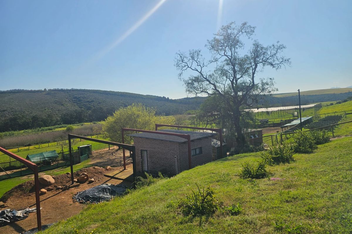 An elevated view of a farm property featuring a brick structure with exposed metal framing, set against a backdrop of rolling hills and open land.
