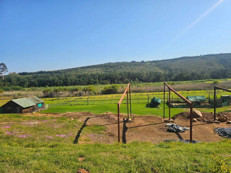 Expansive farm landscape featuring a wooden shed, perimeter fencing, and an unfinished metal structural frame set against a scenic hillside backdrop.